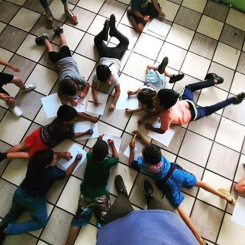 Toma aerea de niños realizando una actividad con cuadernos en el piso en un circulo.
